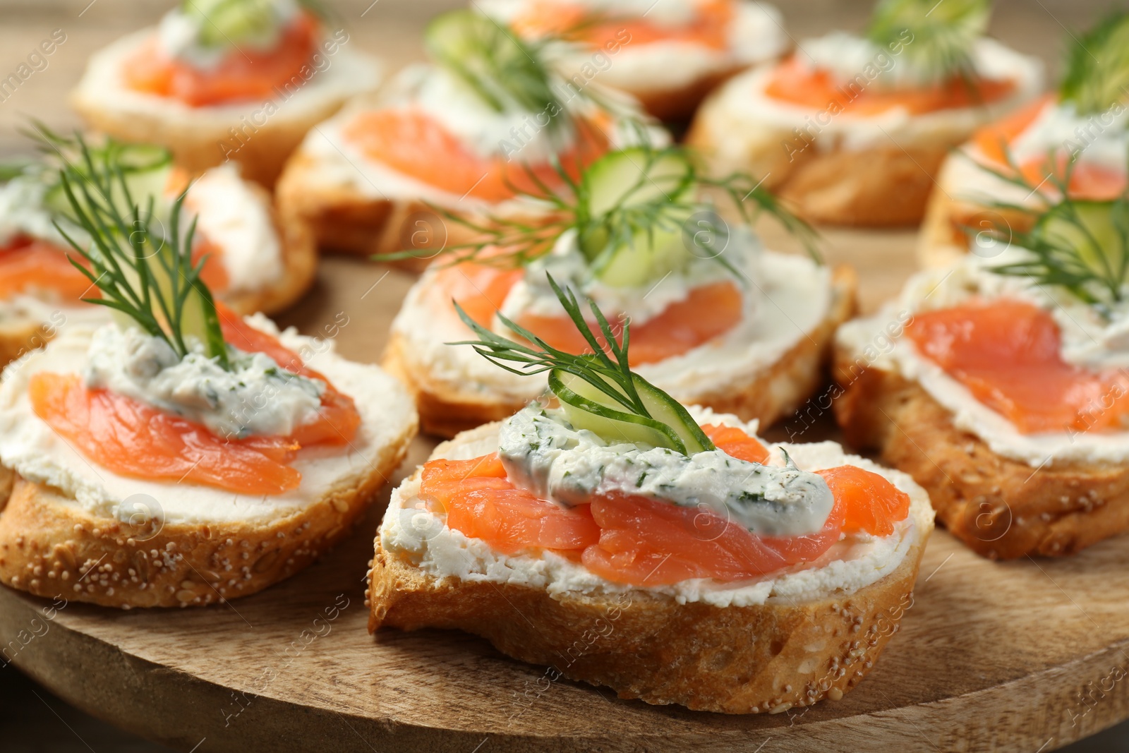 Photo of Tasty canapes with salmon, cucumber, cream cheese and dill on wooden stand, closeup