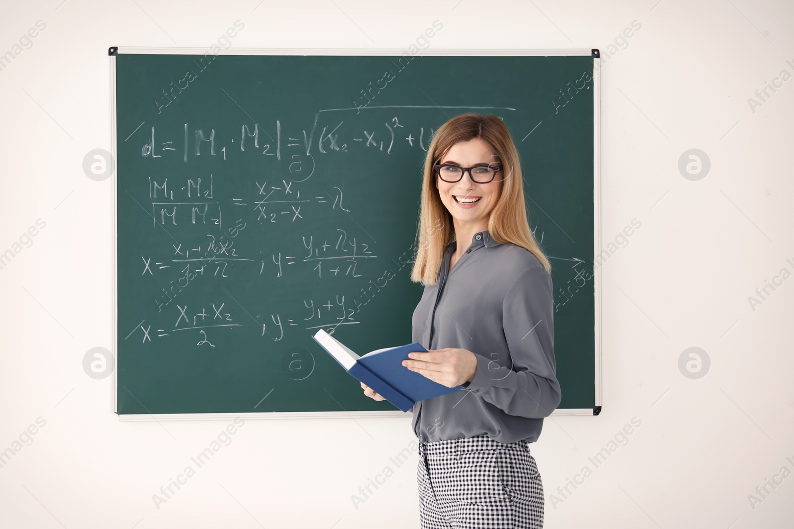 Photo of Female teacher with book standing near blackboard in classroom