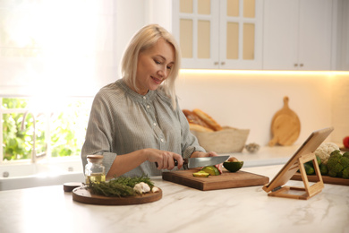 Woman with tablet cooking at table in kitchen