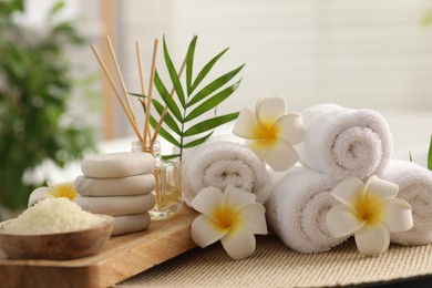 Composition with different spa products, plumeria flowers and palm leaves on table indoors, closeup