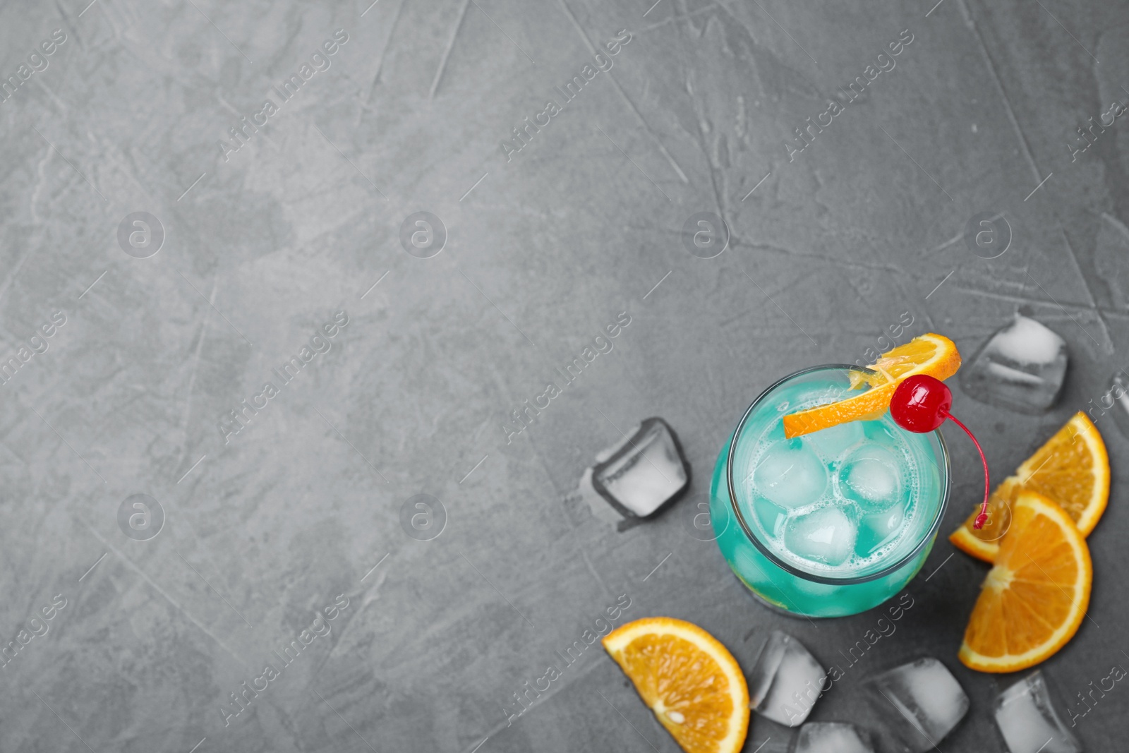 Photo of Glass of tasty refreshing cocktail on grey stone background, flat lay. Space for text