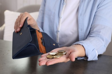 Photo of Poor woman holding coins and empty wallet at grey table indoors, closeup