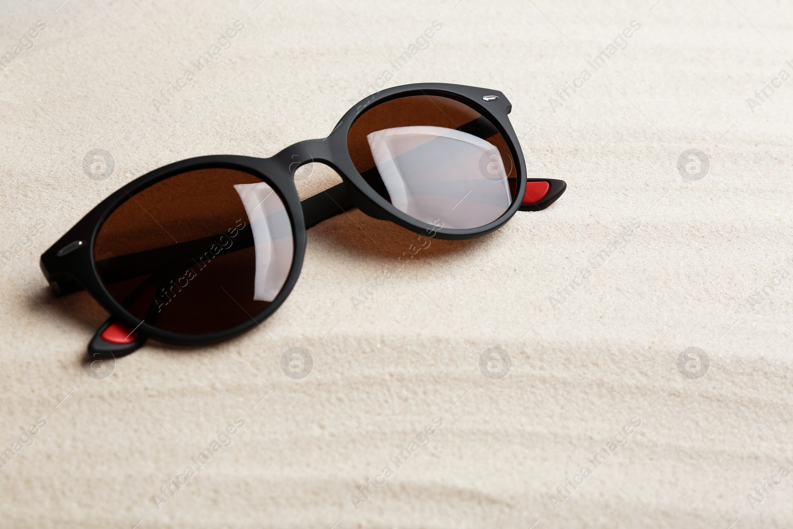 Photo of Stylish sunglasses on white sand. Summer time