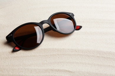 Stylish sunglasses on white sand. Summer time