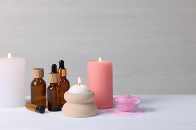 Photo of Different aromatherapy products and burning candles on white wooden table against light background, space for text
