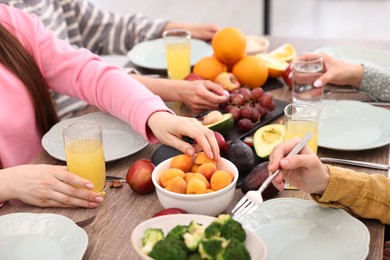 Photo of Friends eating vegetarian food at wooden table indoors, closeup