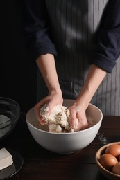 Making bread. Woman kneading dough at wooden table on dark background, closeup