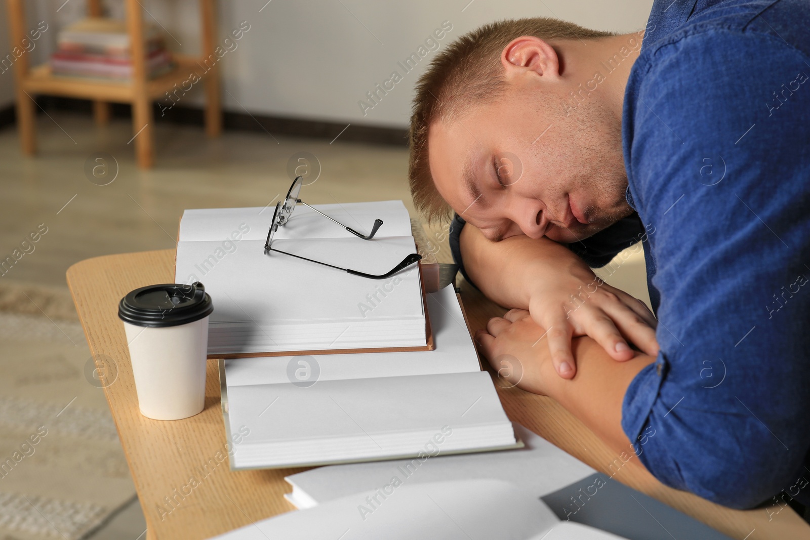 Photo of Tired man sleeping near books at wooden table indoors