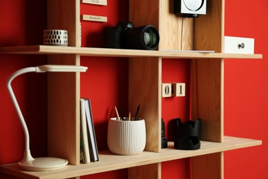 Stylish wooden shelves with photography equipment and decorative elements on red wall