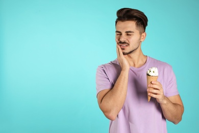 Emotional young man with sensitive teeth and ice cream on color background. Space for text