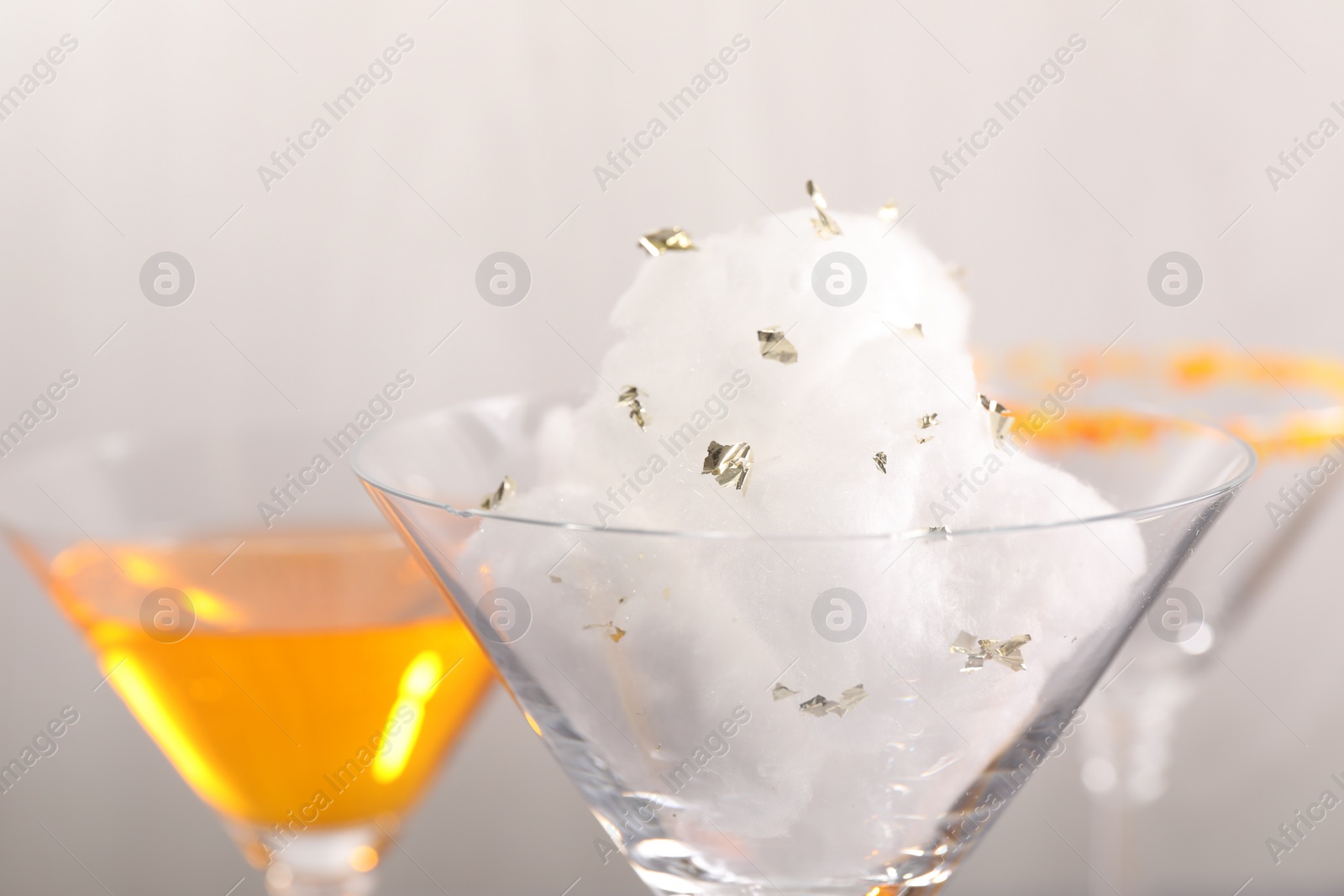 Photo of Tasty cotton candy cocktail in glass and other alcoholic drinks on gray background, closeup