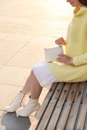 Fashionable young woman with stylish bag on bench outdoors, closeup