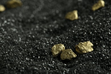Shiny gold nuggets on black sand, closeup. Space for text
