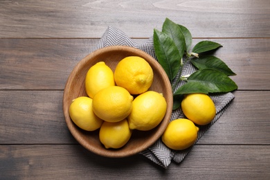 Photo of Many fresh ripe lemons with green leaves on wooden table, flat lay