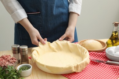 Photo of Woman putting dough for meat pie into baking dish at wooden table, closeup