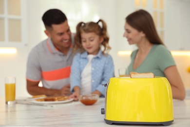 Photo of Happy family having breakfast at table in kitchen, focus on toaster with slices of bread
