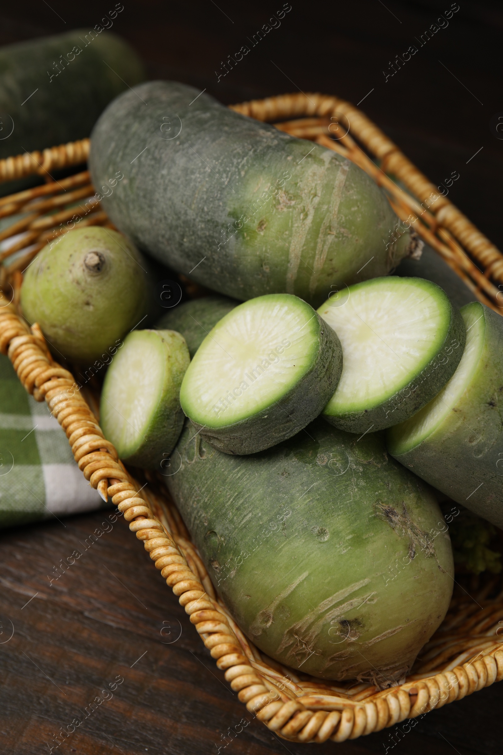 Photo of Green daikon radishes in wicker basket on wooden table, closeup