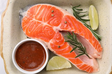 Photo of Fresh fish, lime, rosemary and marinade in baking dish on table, top view