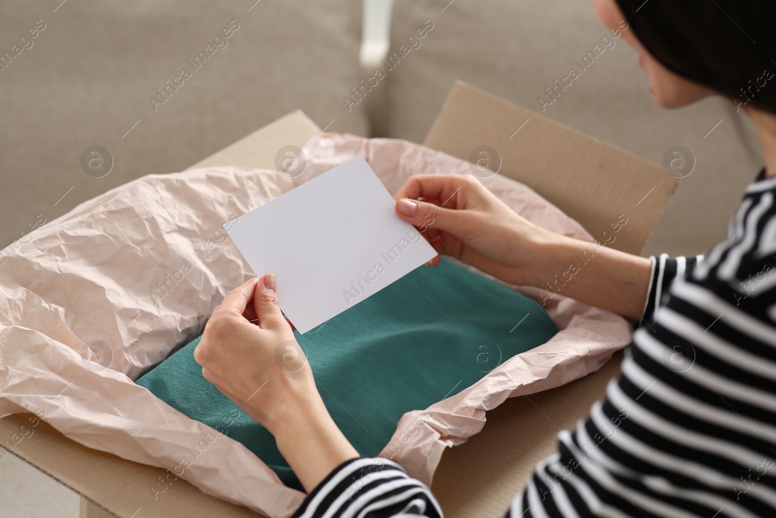 Photo of Woman holding greeting card near parcel with Christmas gift indoors, closeup