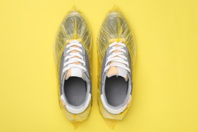 Photo of Sneakers in shoe covers on yellow background, top view