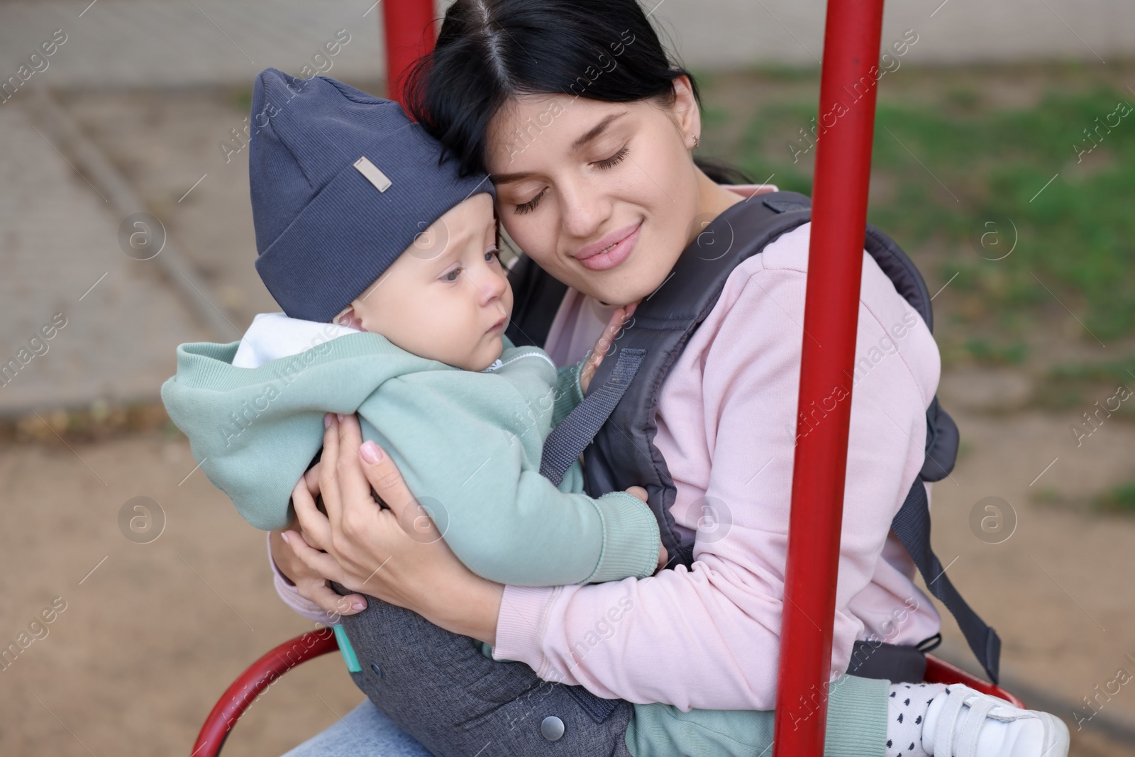 Photo of Mother holding her child in sling (baby carrier) on swing outdoors