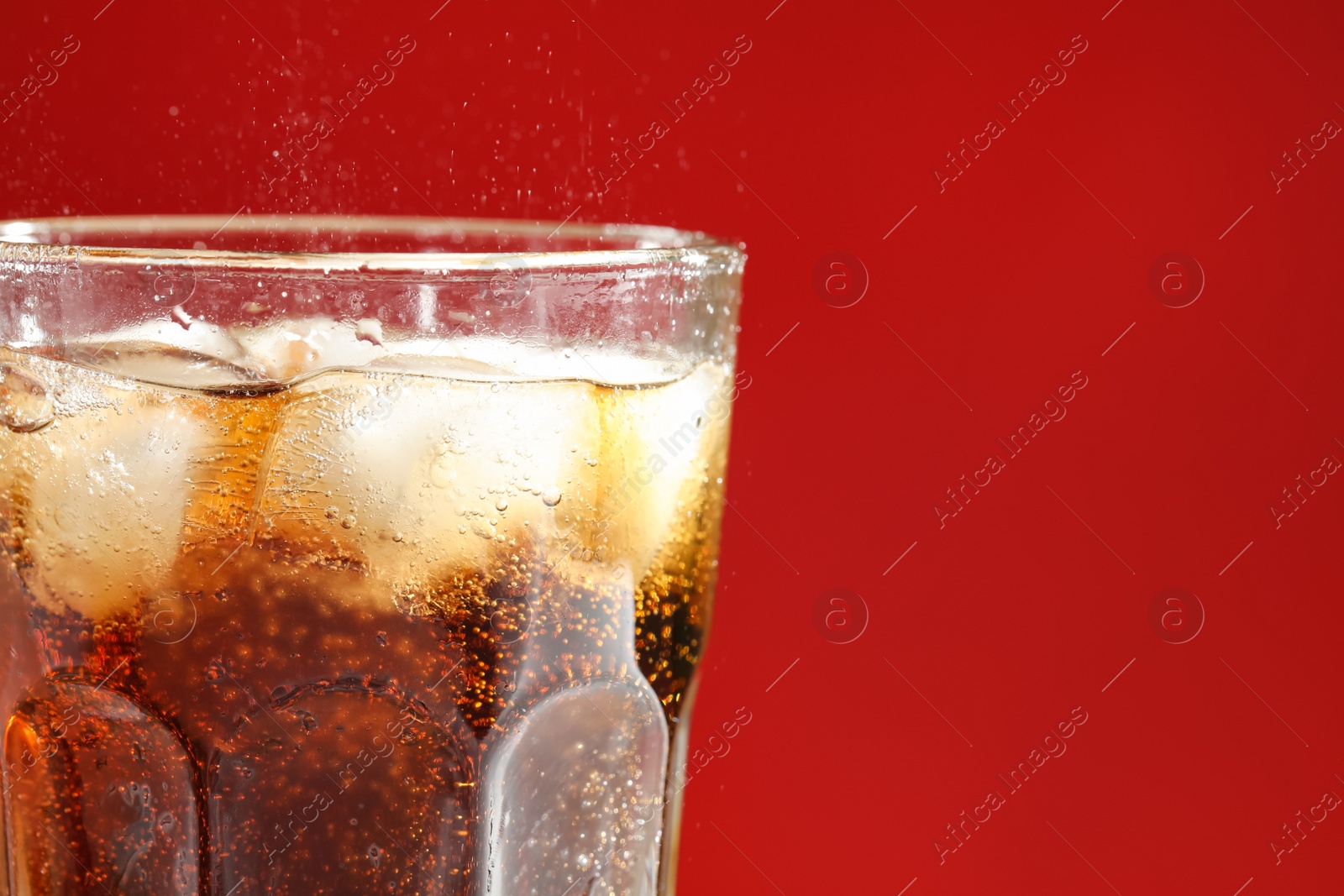 Photo of Glass of refreshing soda drink with ice cubes on red background, closeup. Space for text