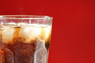 Photo of Glass of refreshing soda drink with ice cubes on red background, closeup. Space for text