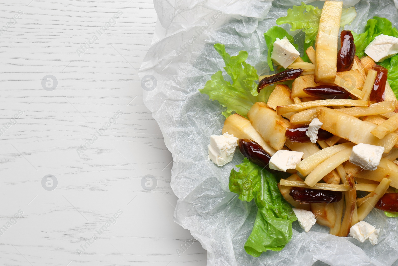 Photo of Delicious parsnip with lettuce, feta cheese and dates on white wooden table, top view. Space for text