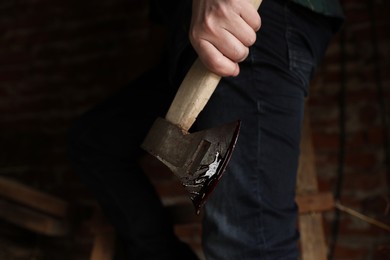 Photo of Man holding bloody axe indoors, closeup view