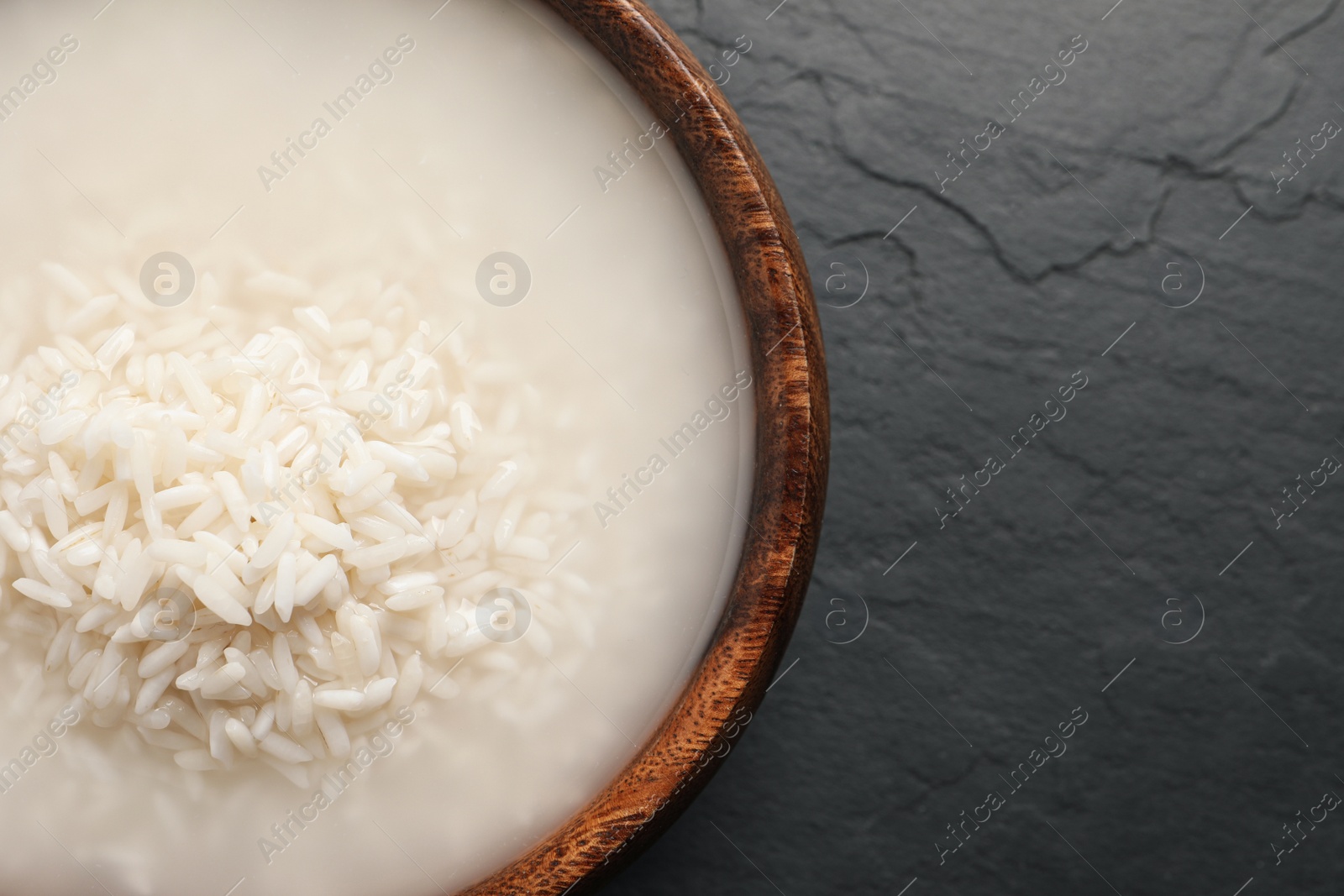 Photo of Rice soaked in water on black table, top view. Space for text