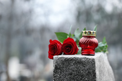 Photo of Red roses and candle on grey granite tombstone outdoors. Funeral ceremony