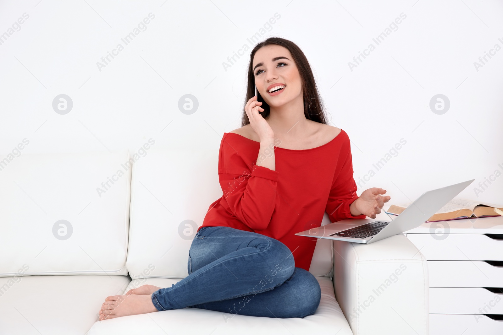 Photo of Attractive young woman talking on mobile phone while using laptop at home