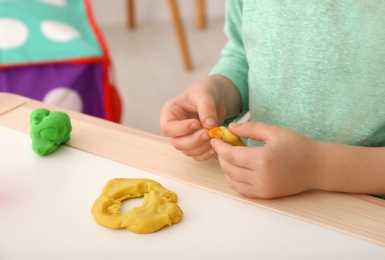 Photo of Cute little child using play dough at table, closeup