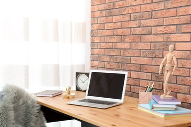 Stylish workplace interior with laptop on table near brick wall. Space for text