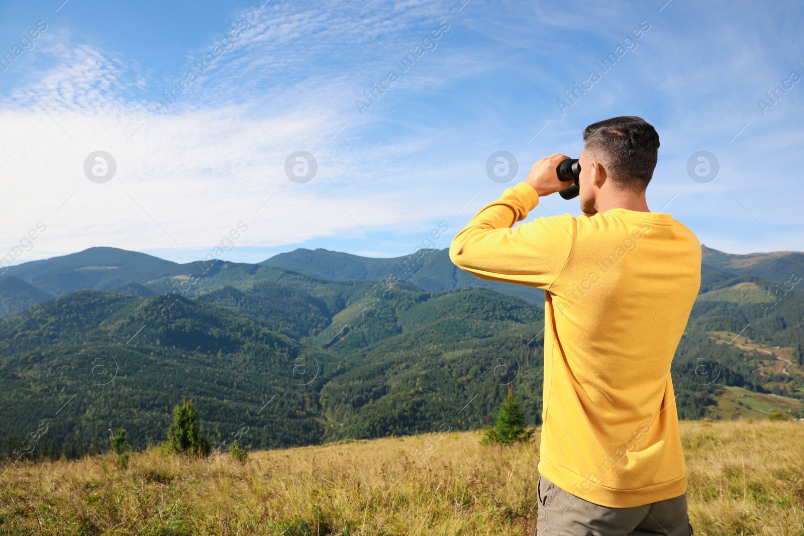 Photo of Man with binoculars in mountains on sunny day, space for text