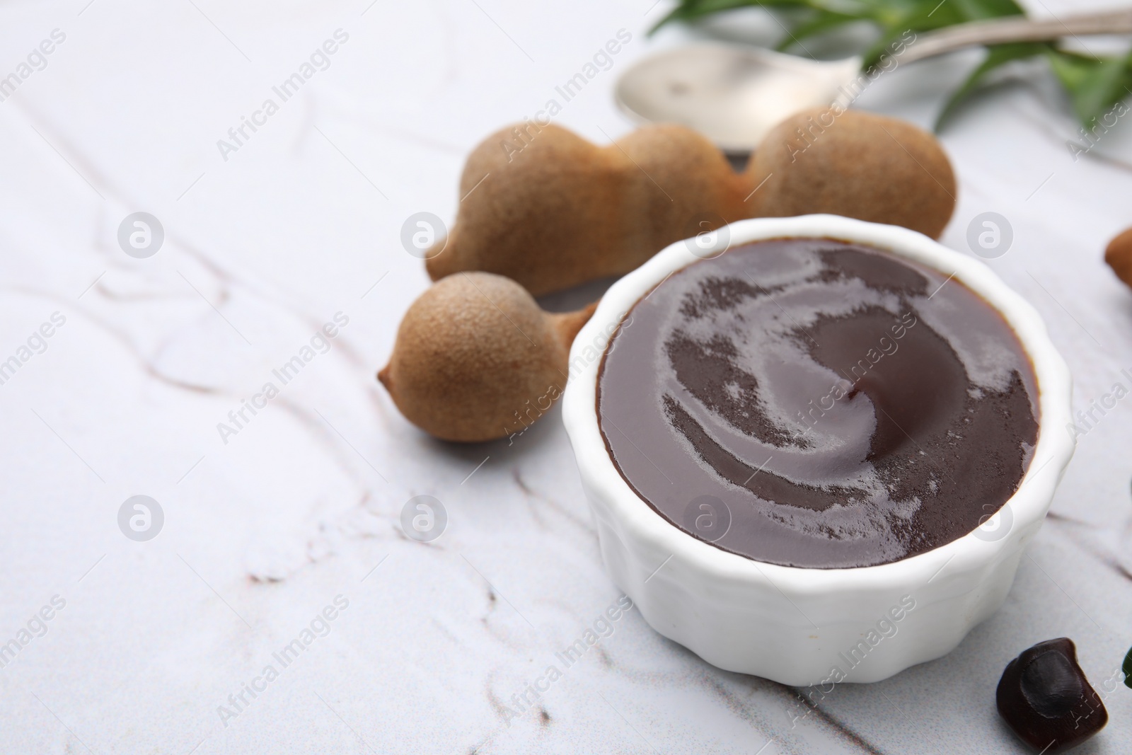 Bowl of tasty tamarind sauce and fresh pods on white textured table. Space for text Photo of Bowl of tasty tamarind sauce and fresh pods on white textured table. Space for text