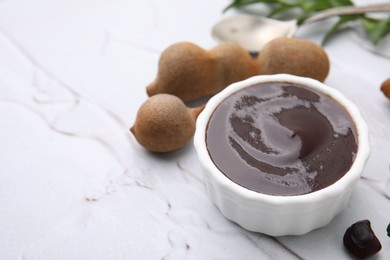 Photo of Bowl of tasty tamarind sauce and fresh pods on white textured table. Space for text