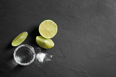 Photo of Mexican Tequila shot, lime slices and salt on black table, flat lay. Space for text