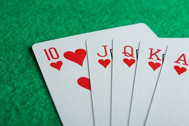 Playing cards with royal flush combination on green table, closeup