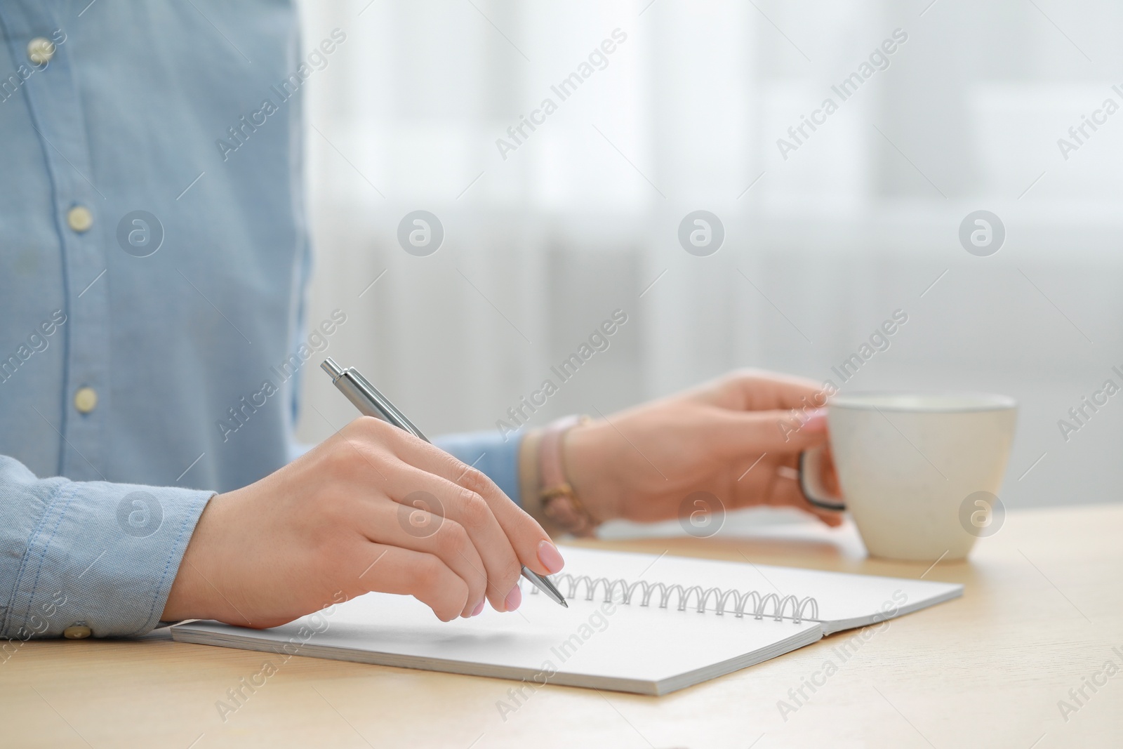 Photo of Woman writing in notebook at wooden table, closeup