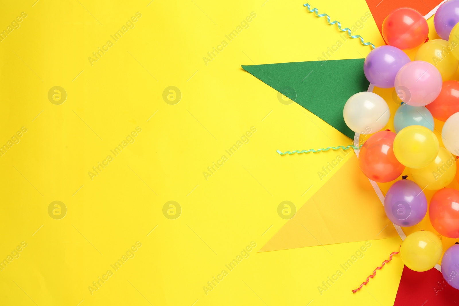 Photo of Bunting with colorful triangular flags and other festive decor on yellow background, flat lay. Space for text