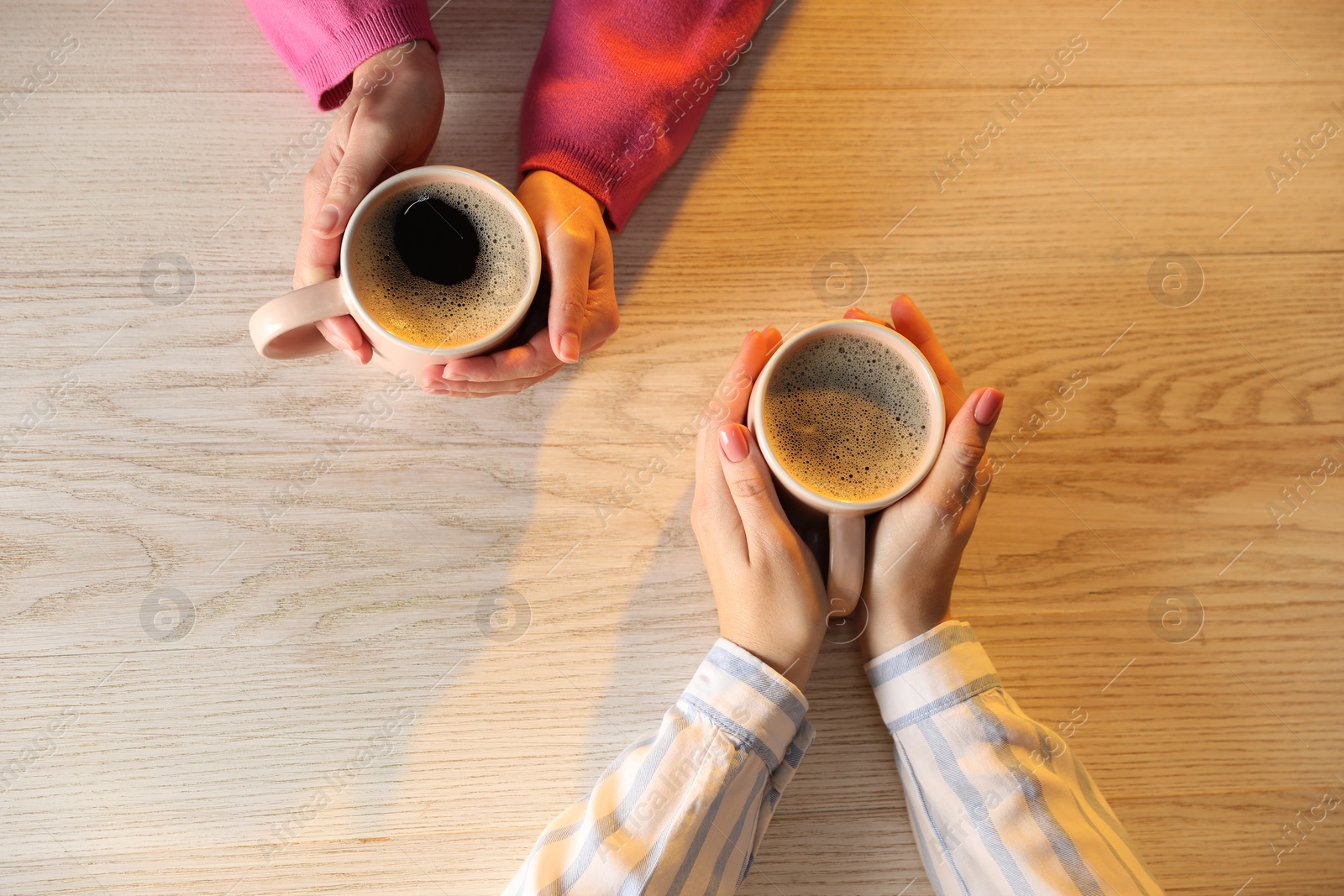 Photo of Women with cups of hot coffee at light wooden table, top view