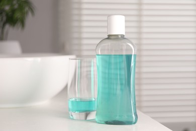 Photo of Bottle and glass of mouthwash on white countertop in bathroom