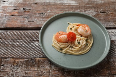 Photo of Heart made of tasty spaghetti, tomato, shrimps and cheese on wooden table. Space for text