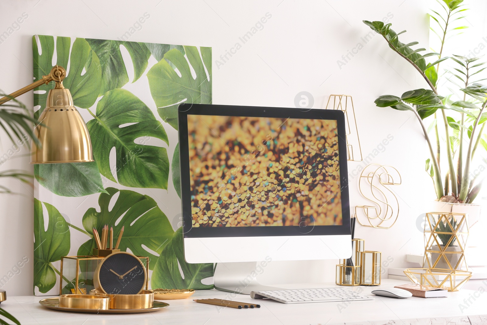 Photo of Modern workplace with computer and golden decor on desk near wall. Stylish interior design