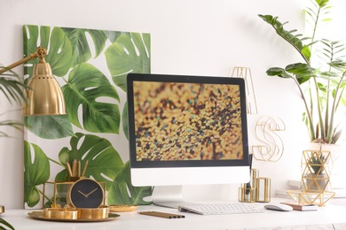 Modern workplace with computer and golden decor on desk near wall. Stylish interior design