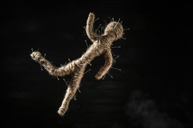 Voodoo doll with pins on black wooden background