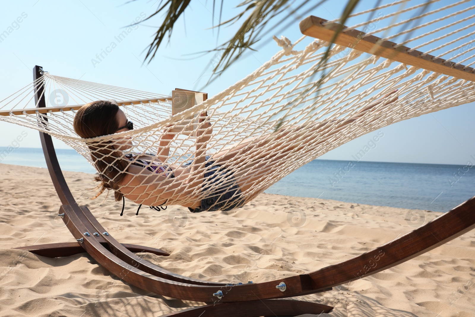 Photo of Young woman reading book in hammock on beach