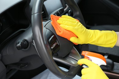 Photo of Woman cleaning steering wheel with rag in car, closeup