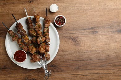 Photo of Metal skewers with delicious meat, ketchup and spices served on wooden table, flat lay. Space for text